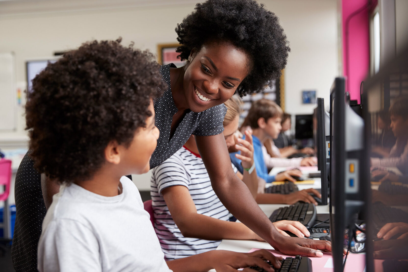 Teacher smiling and talking to a student who is using a computer