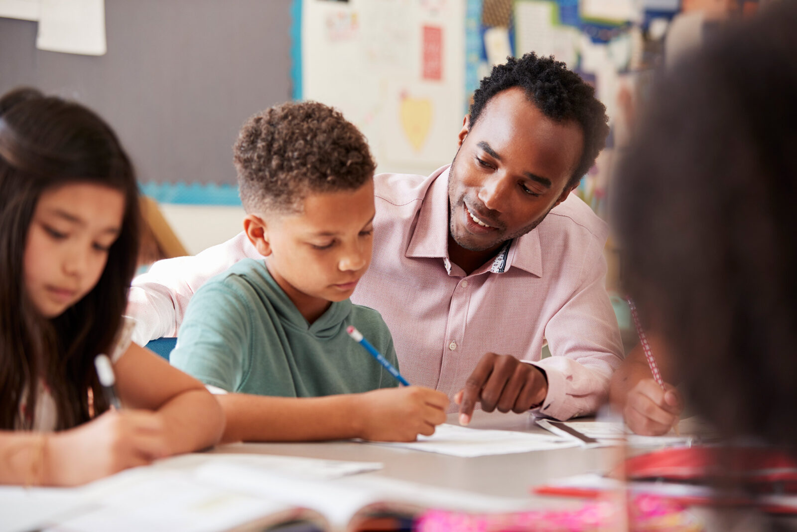 Teacher helping a student who is writing something with a pencil